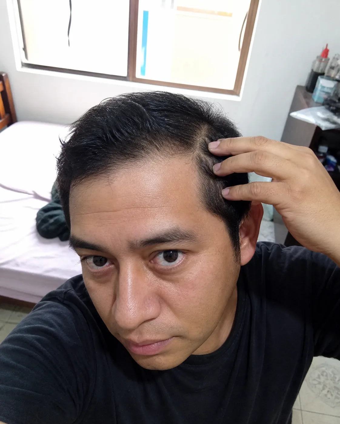 Selfie casual de un hombre separando el cabello cerca de la sien en su dormitorio